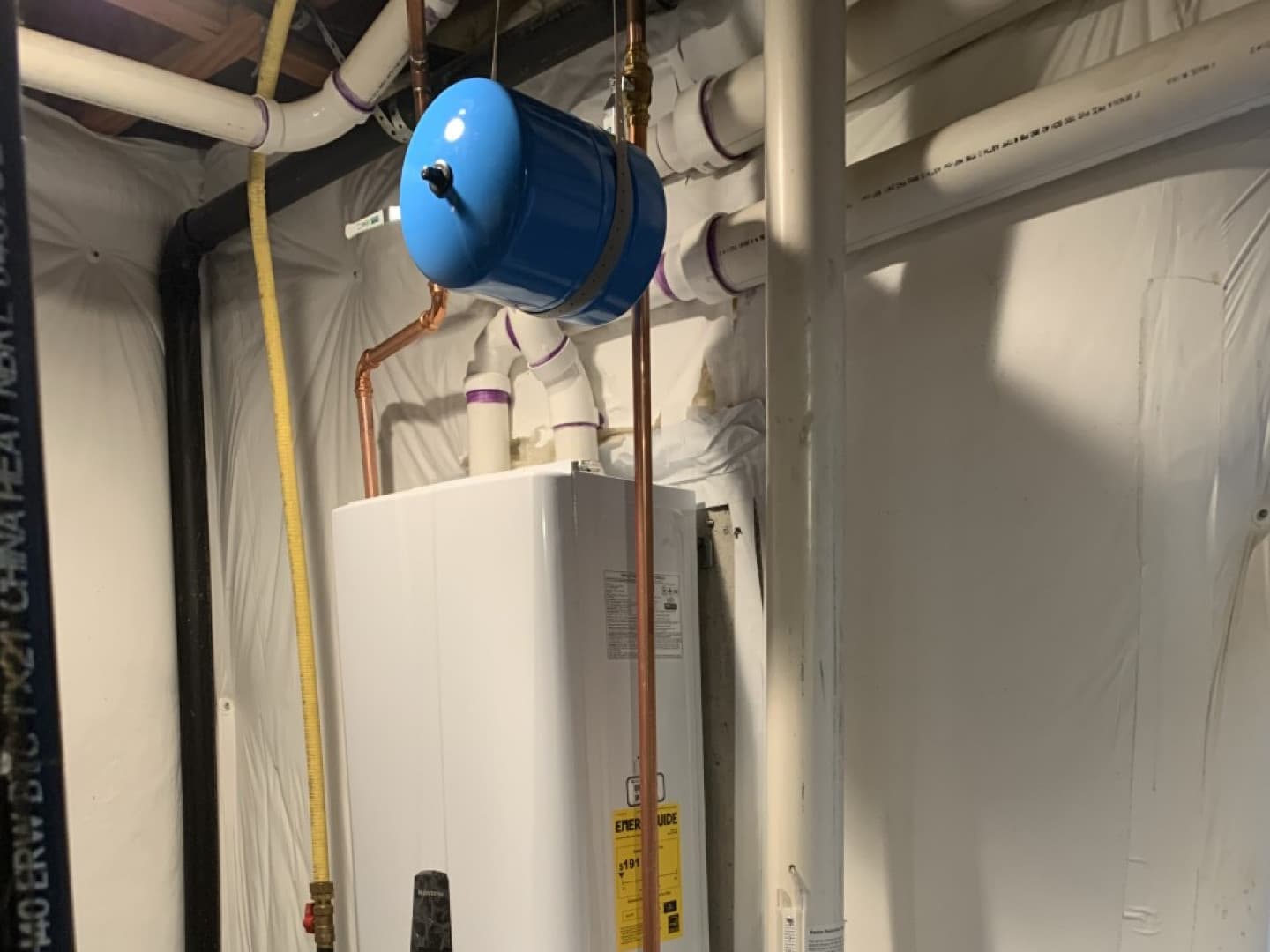 Tankless water heater with a blue expansion tank and new copper lines, installed in a basement